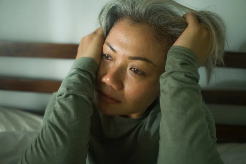 An older woman with her head in her hands with an upset expression.